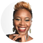 A portrait of a smiling woman with a stylish short, blonde-tipped hairstyle and large silver earrings. She wears a silver necklace and her makeup includes glossy red lipstick, capturing the contemporary Los Angeles aesthetic.