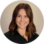 Headshot of a smiling woman with medium-length brown hair, wearing a black blouse, against a light beige background in LA.