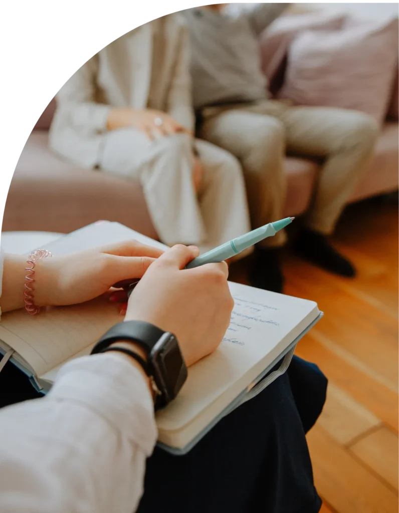 At the Avedian Counseling Center, a person diligently takes notes with a pen in a notebook, as two others converse comfortably on the sofa in the background.