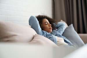 Woman with curly hair resting on a couch to restore her energy. She is practicing physical rest.