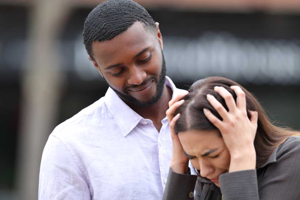 A woman holding her head in distress while a man looks on, representing dating anxiety and the attachment system being activated.