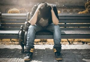 A person is sitting on a bench, leaning forward with their head in their hands, appearing distressed or upset.