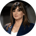 A woman with straight brown hair and bangs, wearing a navy blazer and white top, poses for a professional headshot against a dark background.