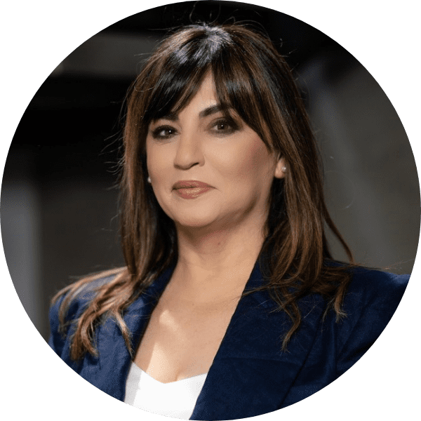 A woman with straight brown hair and bangs, wearing a navy blazer and white top, poses for a professional headshot against a dark background.